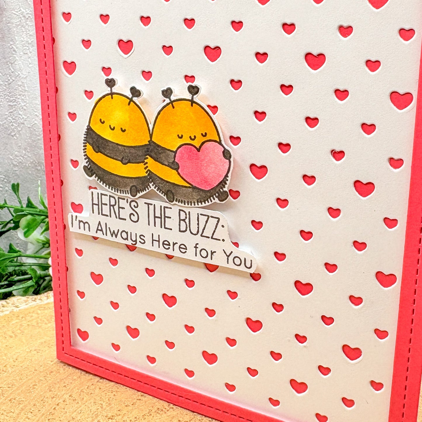 Card with two bees holding a heart and text on a background with red hearts.