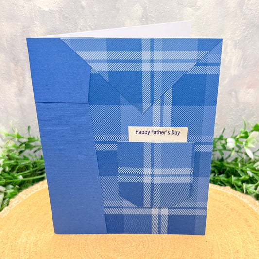Blue plaid Father's Day card on a textured surface with greenery in the background
