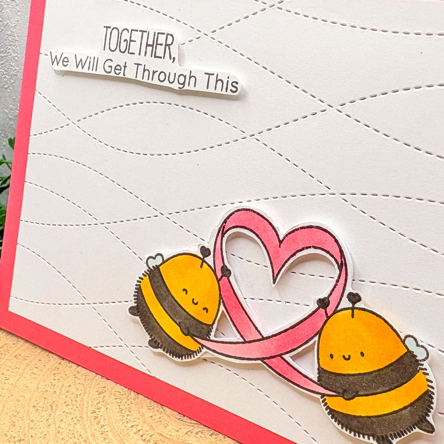 Card with two bees and a pink ribbon forming a heart, with text 'Together, we will get through this' on a white background.