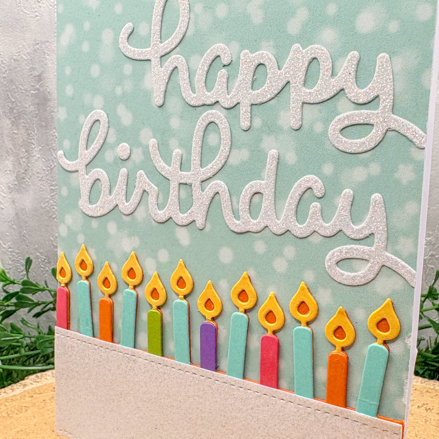 Birthday card with colorful candles and 'happy birthday' text on a light blue background.