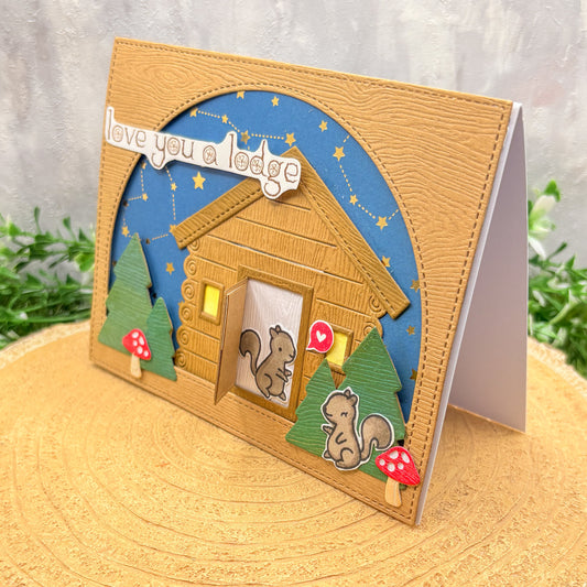 Greeting card with a wooden cabin design, squirrels, and 'love you a lodge' text on a textured surface.