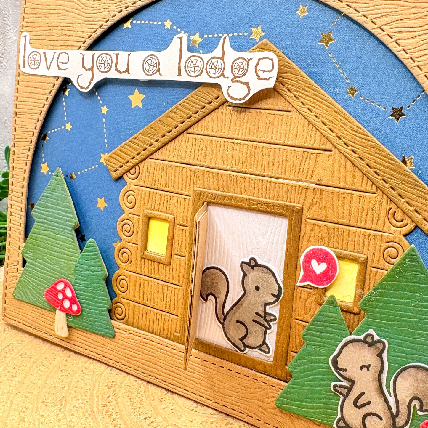 Wooden cabin with a squirrel and trees, featuring 'love you a lodge' text.