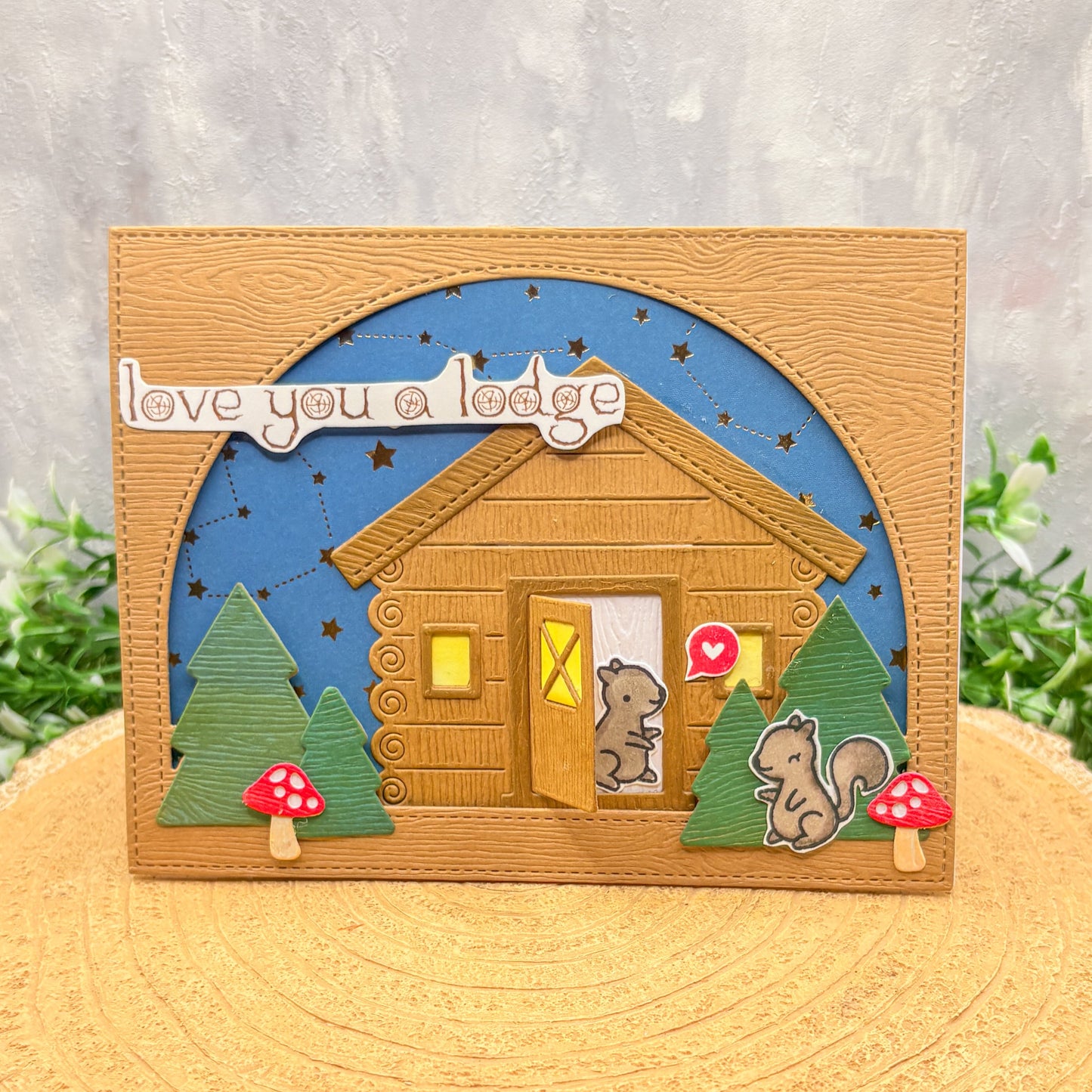 Card with a wooden cabin, trees, and a squirrel design, featuring the text 'love you a lodge'.