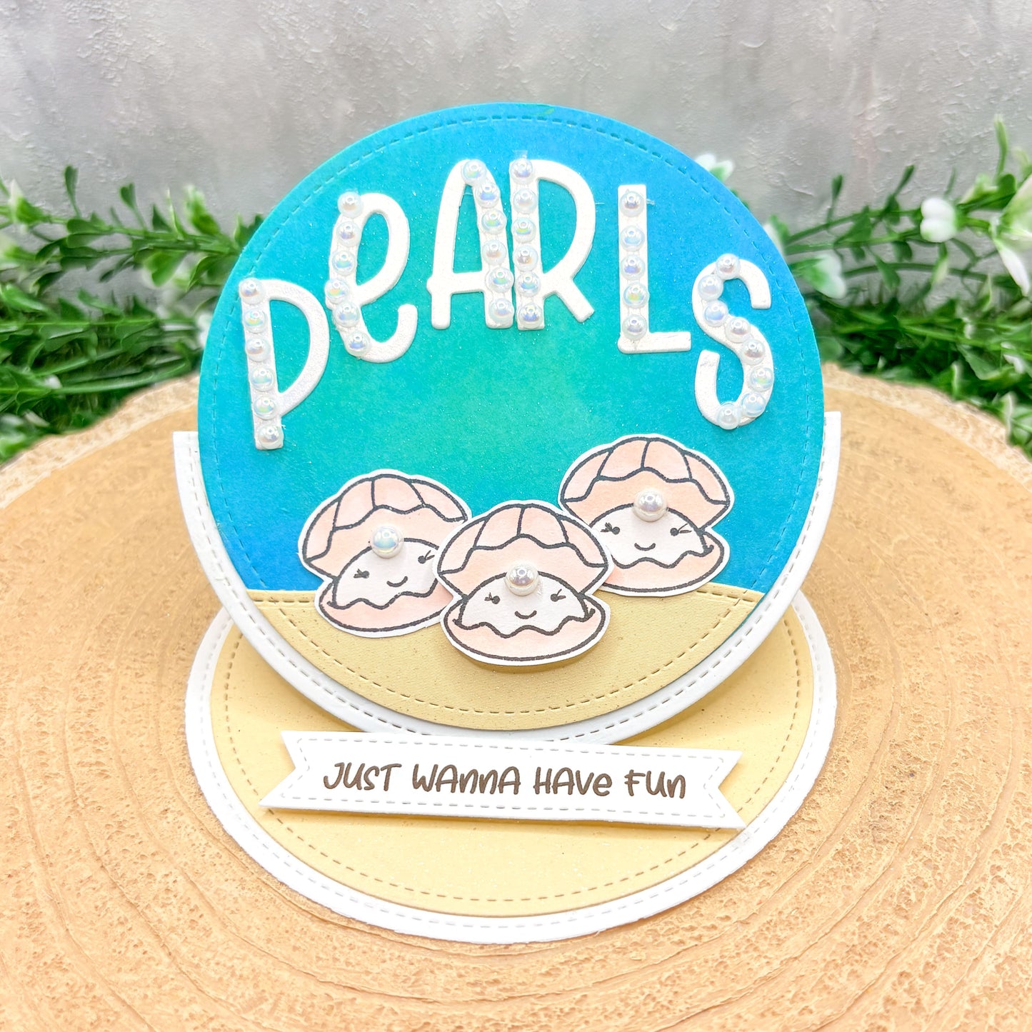 Circular card with 'PEARLS' text and shell designs on a textured surface.