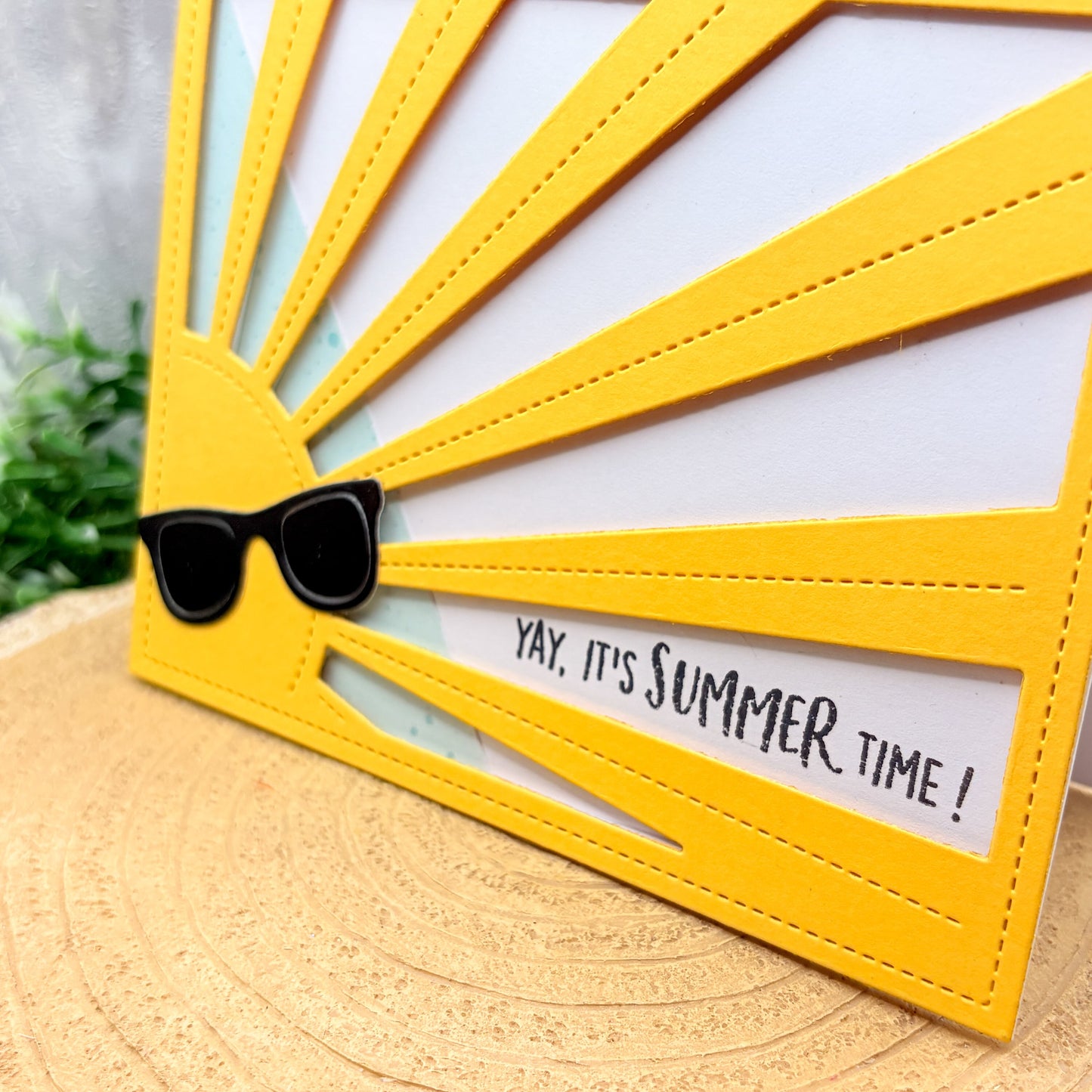 Yellow sun-shaped card with sunglasses and 'Yay, it's summer time!' text on a wooden surface.