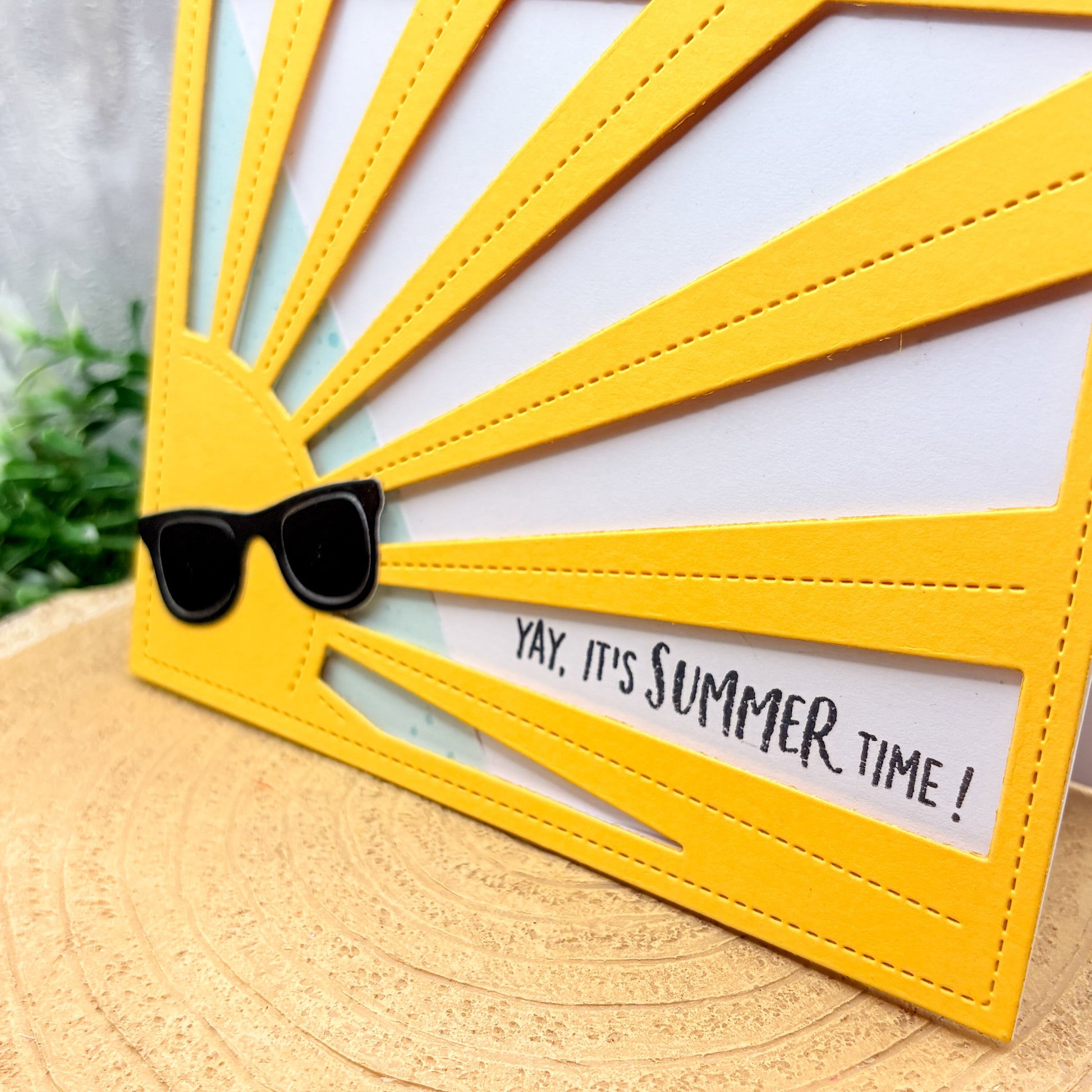 Yellow sun-shaped card with sunglasses and 'Yay, it's summer time!' text on a wooden surface.