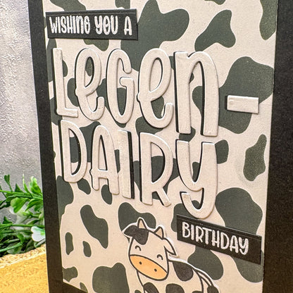 Birthday card with cow pattern and text 'Wishing you a legen-dairy birthday' on a camouflage background.