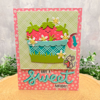 Colorful birthday card with strawberry design and text 'Have a sweet birthday!' on a floral-patterned surface.