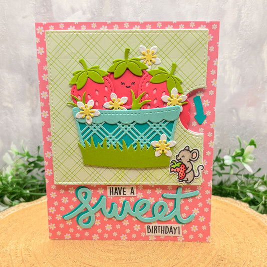 Colorful birthday card with strawberry design and text 'Have a sweet birthday!' on a floral-patterned surface.