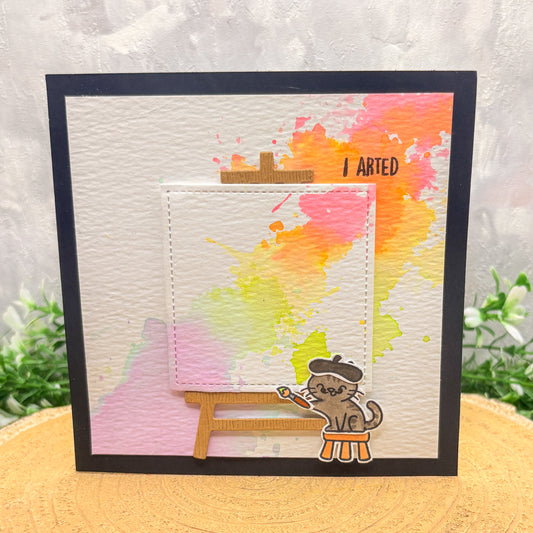 Card with a cat painting and watercolor background on a wooden surface.