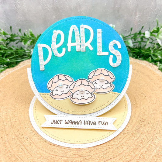 Circular card with 'PEARLS' text and shell designs on a textured surface.
